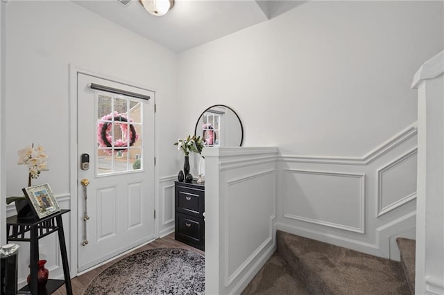 entryway featuring a decorative wall, stairway, and wainscoting