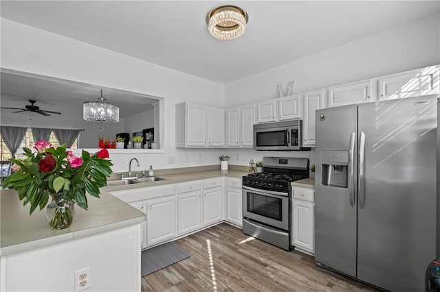 kitchen featuring white cabinets, wood finished floors, light countertops, a sink, and stainless steel appliances