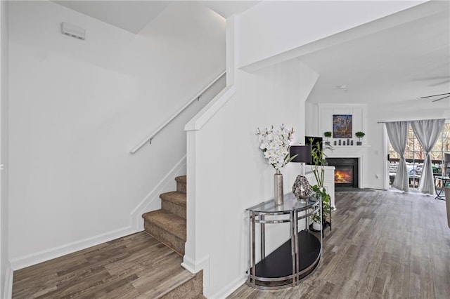 stairway with baseboards, a ceiling fan, a glass covered fireplace, and wood finished floors