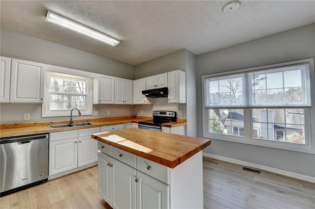 kitchen featuring stainless steel appliances, wooden counters, under cabinet range hood, and a sink