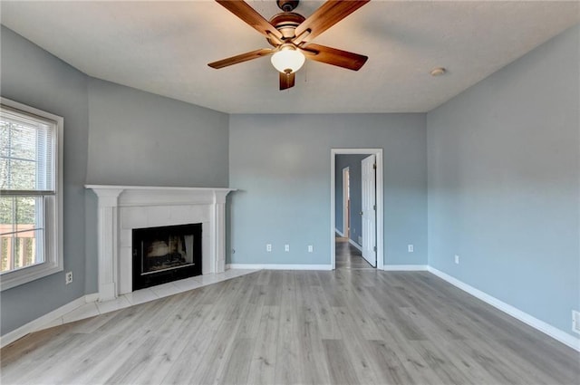 unfurnished living room featuring ceiling fan, a fireplace, baseboards, and wood finished floors