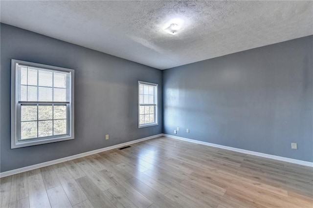 spare room with a textured ceiling, wood finished floors, visible vents, and baseboards