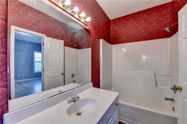 bathroom with a textured ceiling, shower / tub combination, vanity, and wallpapered walls