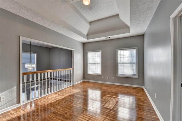 spare room with a textured ceiling, hardwood / wood-style flooring, ceiling fan with notable chandelier, baseboards, and a raised ceiling