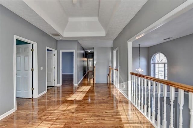 corridor with baseboards, wood finished floors, an inviting chandelier, a tray ceiling, and a textured ceiling