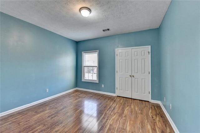 unfurnished bedroom featuring a closet, visible vents, a textured ceiling, wood finished floors, and baseboards