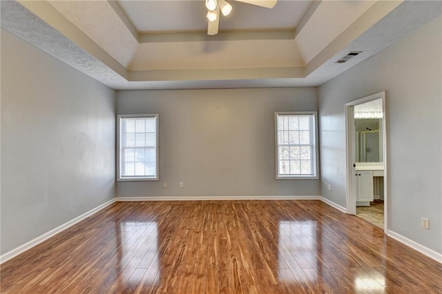 empty room featuring hardwood / wood-style floors, a tray ceiling, visible vents, and baseboards