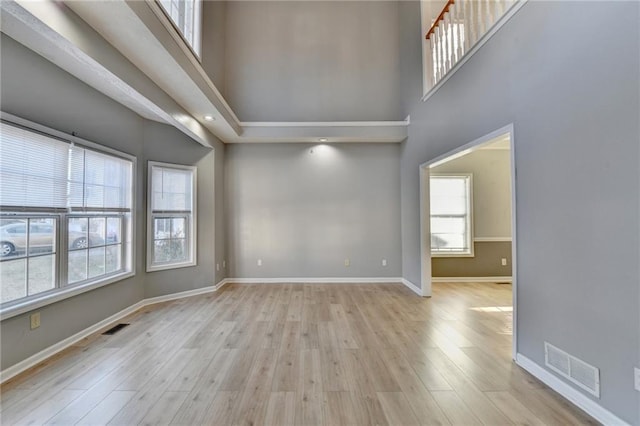 unfurnished room featuring a towering ceiling, baseboards, visible vents, and wood finished floors