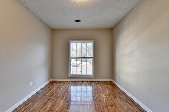 empty room with a textured ceiling, wood finished floors, visible vents, and baseboards