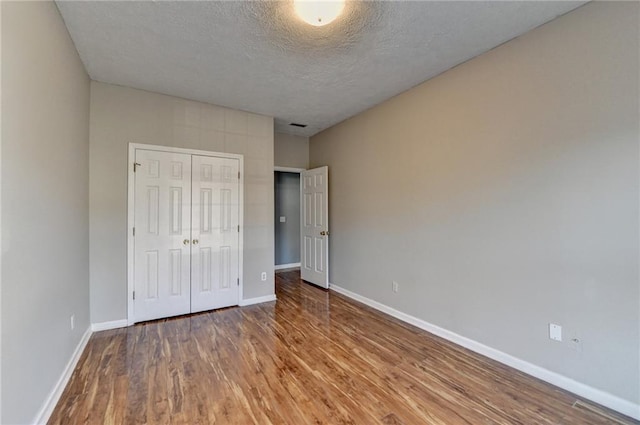 unfurnished bedroom with a textured ceiling, a closet, baseboards, and wood finished floors