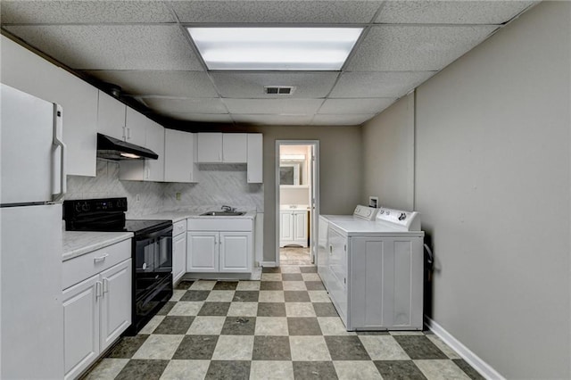 kitchen featuring freestanding refrigerator, washer and dryer, under cabinet range hood, black / electric stove, and tile patterned floors