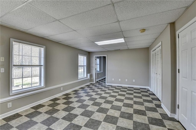 unfurnished room featuring dark floors, a drop ceiling, and baseboards