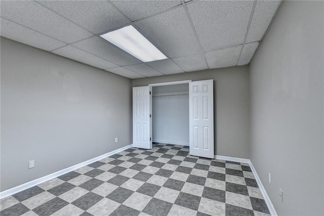 unfurnished bedroom with dark floors, a paneled ceiling, and baseboards