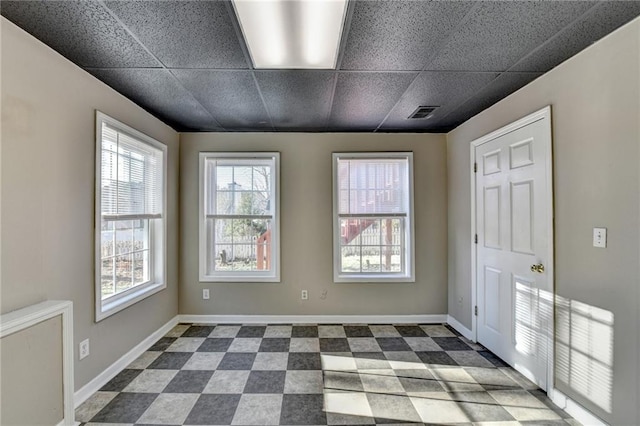 spare room with dark floors, a drop ceiling, and baseboards