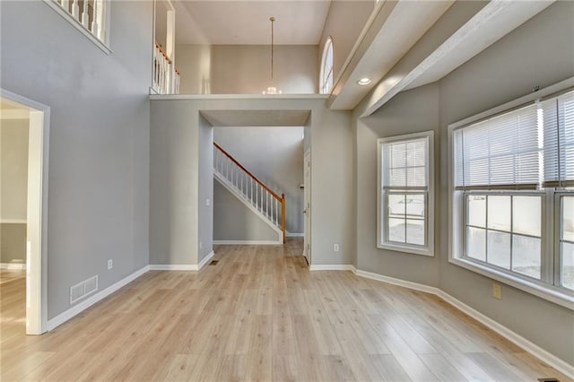 unfurnished living room with wood finished floors, a towering ceiling, visible vents, stairs, and baseboards