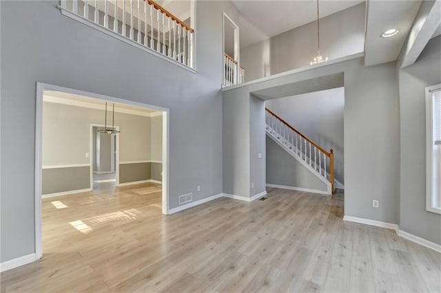 unfurnished living room with baseboards, a towering ceiling, stairway, wood finished floors, and an inviting chandelier