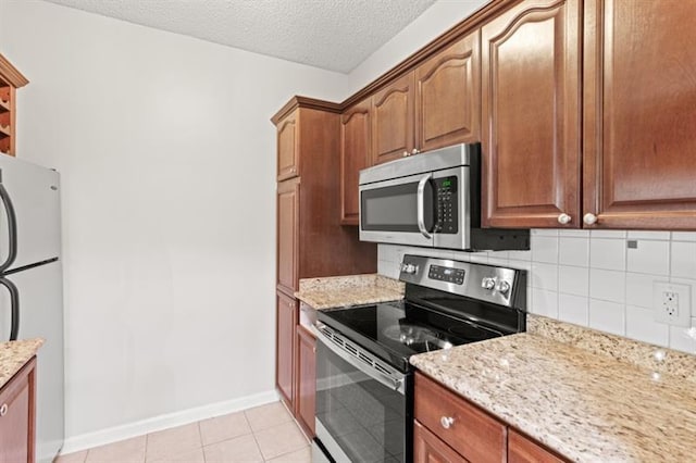 kitchen featuring light tile patterned floors, a textured ceiling, appliances with stainless steel finishes, tasteful backsplash, and light stone counters