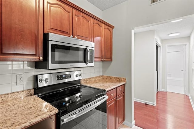 kitchen featuring decorative backsplash, light wood-type flooring, light stone counters, a textured ceiling, and stainless steel appliances