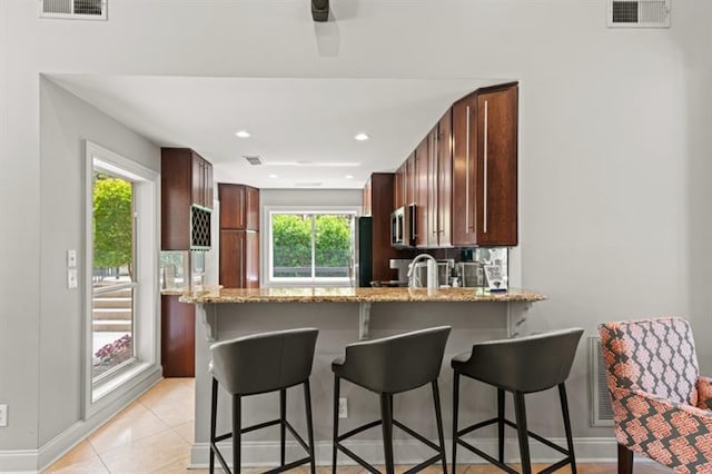 kitchen featuring stainless steel appliances, light stone countertops, a breakfast bar area, and a healthy amount of sunlight