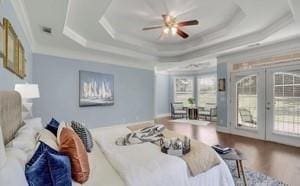 bedroom featuring hardwood / wood-style floors, ornamental molding, access to outside, a raised ceiling, and french doors