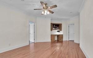 unfurnished living room with wood-type flooring, crown molding, built in desk, and ceiling fan