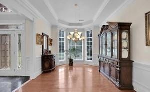 unfurnished dining area featuring hardwood / wood-style flooring, ornamental molding, a notable chandelier, and a tray ceiling