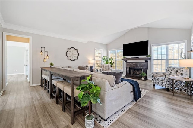 living area featuring plenty of natural light, a fireplace with raised hearth, light wood-type flooring, and vaulted ceiling