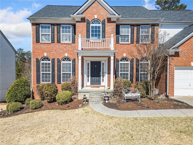 colonial inspired home with a front yard, a balcony, and brick siding