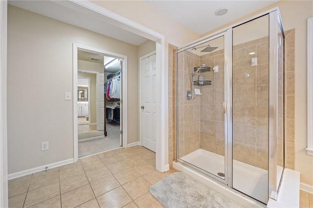 full bath featuring tile patterned floors, a spacious closet, baseboards, and a stall shower