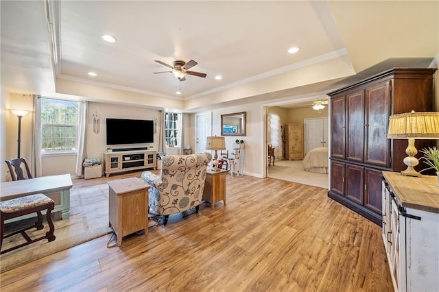 living room with a tray ceiling, ceiling fan, ornamental molding, and light wood-style flooring