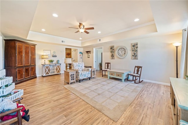 living room with a raised ceiling, a ceiling fan, light wood finished floors, and ornamental molding