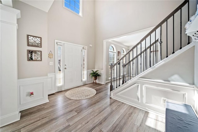 foyer entrance featuring stairs, wainscoting, a high ceiling, wood finished floors, and a decorative wall