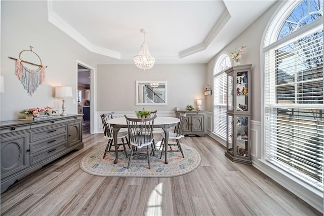 dining room featuring light wood finished floors, crown molding, a wainscoted wall, a tray ceiling, and a notable chandelier