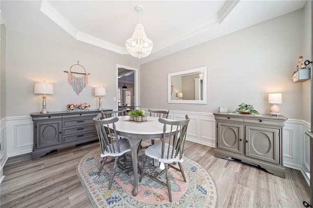 dining area featuring light wood-type flooring, a wainscoted wall, a notable chandelier, crown molding, and a decorative wall