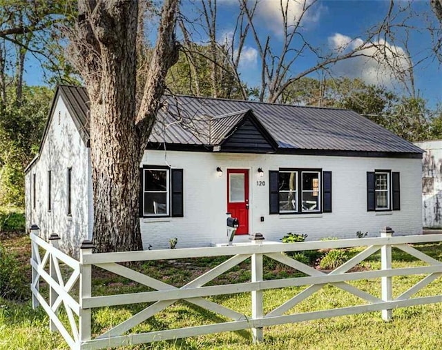 ranch-style home featuring a fenced front yard, metal roof, and brick siding