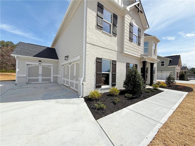 view of front of home featuring an attached garage, roof with shingles, concrete driveway, and brick siding