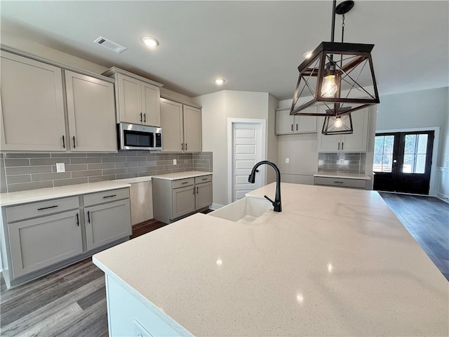 kitchen featuring wood finished floors, gray cabinets, stainless steel microwave, and a sink