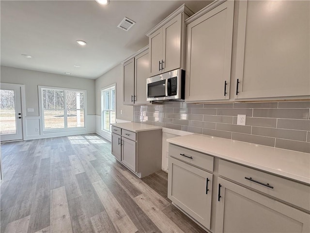 kitchen with visible vents, light countertops, light wood finished floors, stainless steel microwave, and tasteful backsplash