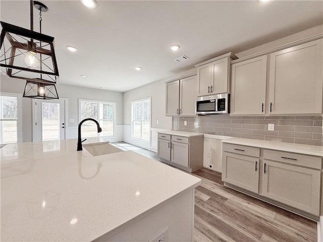 kitchen featuring tasteful backsplash, visible vents, stainless steel microwave, light wood-type flooring, and a sink