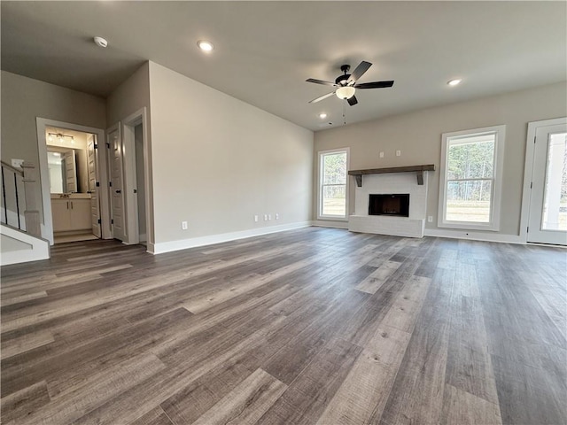 unfurnished living room with a brick fireplace, a healthy amount of sunlight, stairway, and wood finished floors