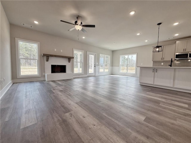 unfurnished living room with a fireplace with raised hearth, recessed lighting, wood finished floors, a ceiling fan, and visible vents