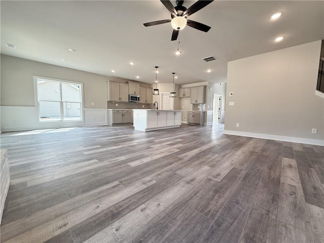 unfurnished living room featuring ceiling fan, recessed lighting, wood finished floors, a sink, and visible vents