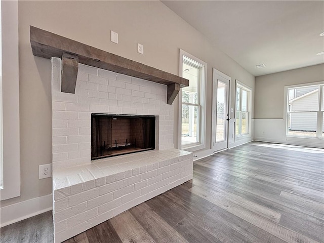 unfurnished living room featuring wainscoting, a fireplace, baseboards, and wood finished floors