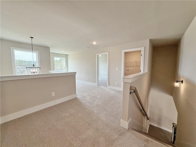 spare room with an inviting chandelier, baseboards, and light colored carpet