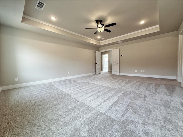 empty room featuring a tray ceiling, visible vents, light carpet, and baseboards