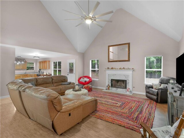 living area featuring a ceiling fan, high vaulted ceiling, baseboards, light wood-style flooring, and a premium fireplace