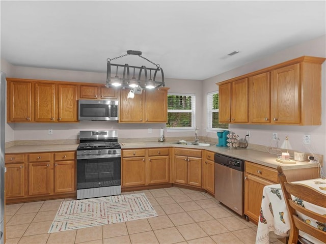 kitchen with a sink, appliances with stainless steel finishes, light tile patterned flooring, and light countertops