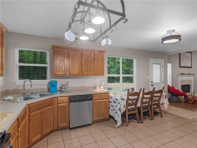 kitchen with stainless steel dishwasher, light countertops, brown cabinets, a sink, and light tile patterned floors
