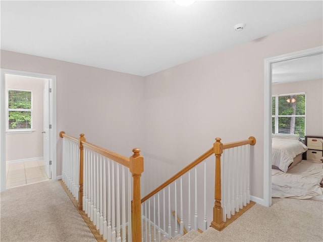 hallway featuring baseboards, carpet, and an upstairs landing