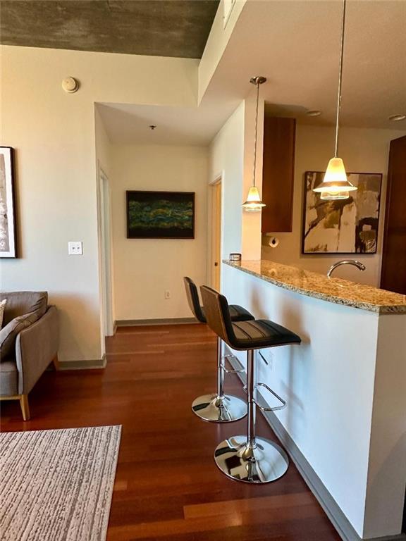 855 Peachtree St NE Unit 1406, Atlanta, GA 30308 - kitchen with dark wood-type flooring, baseboards, light stone counters, a kitchen breakfast bar, and hanging light fixtures